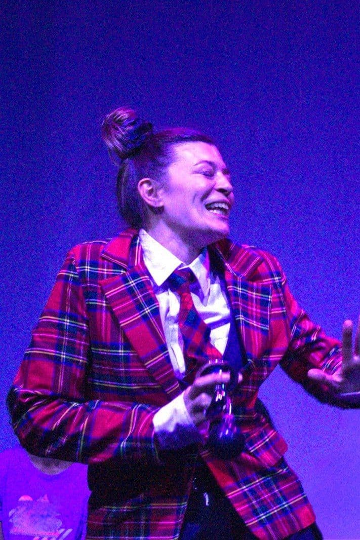 Una intérprete con saco escocés sonriendo sobre un fondo azul, en Circo transatlántico
